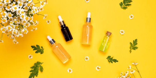 Glasflaschen mit Essenz oder Serum mit Kamillenblüten. Feuchtigkeitsspendende Gesichtscreme und Kamille auf gelbem Hintergrund - Foto, Bild