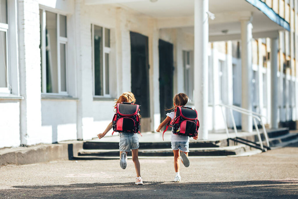 Twee schoolmeisjes die elkaars handen vasthouden rennen naar school, terug naar school, basisonderwijs voor kinderen. - Foto, afbeelding
