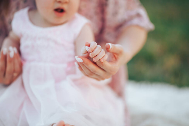 Kleines Neugeborenes im rosa Kleid mit Mama auf weißem Plaid in einem Park. - Foto, Bild