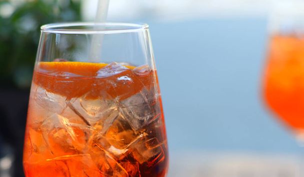 Iced bright orange drink with straw, orange peel and ice cubes in transparent glass. Selective focus - Φωτογραφία, εικόνα