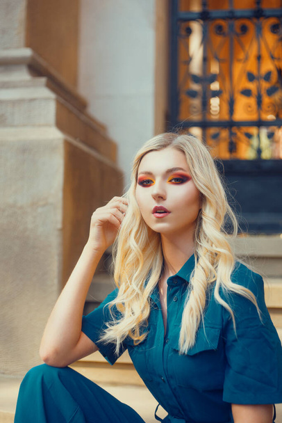 Blonde with beautiful smoky eyes makeup. Bright red shadows on a beautiful female face. A model on the street sits near the university in a suit. Fashion - Foto, imagen