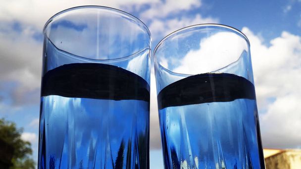 deux verres bleus remplis d'eau avec perspective unique et ciel nuageux en arrière-plan - Photo, image