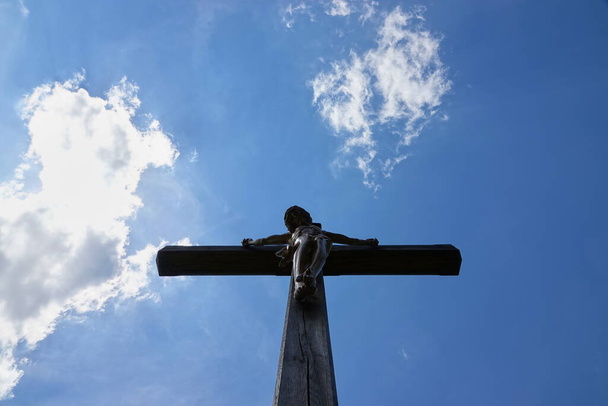 Figura de Jesús (cruci fixus) en cruz de madera marrón. Cielo azul con nubes blancas. Alemania
. - Foto, Imagen