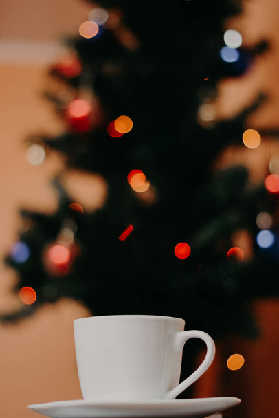 Taza de café de color blanco con árbol de Navidad en el fondo
  - Foto, imagen