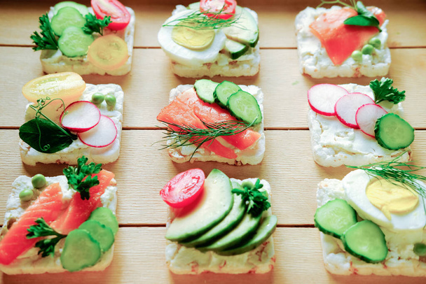 healthy sandwiches with rice crispy bread and various toppings. healthy ingredients for dinner start. appetizers on a wooden table. smoked salmon and avocado sandwiches. fresh ingredients. - Valokuva, kuva