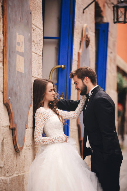 Esküvői pár ölelkezik az óvárosban. Kék évjárat ajtók és kávézó az ősi városban a háttérben. stílusos menyasszony fehér hosszú ruha és vőlegény öltöny és csokornyakkendő. esküvő napja. - Fotó, kép