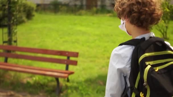 The schoolboy has put the mask on his chin and breathes while sitting on a bench in the schoolyard. New school year during the covid-19 coronavirus pandemic - Filmmaterial, Video