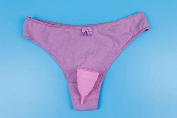 Pantalón de mujer con copa menstrual sobre fondo azul pastel. Vista superior. Concepto de días críticos, menstruación, higiene femenina
 - Foto, imagen