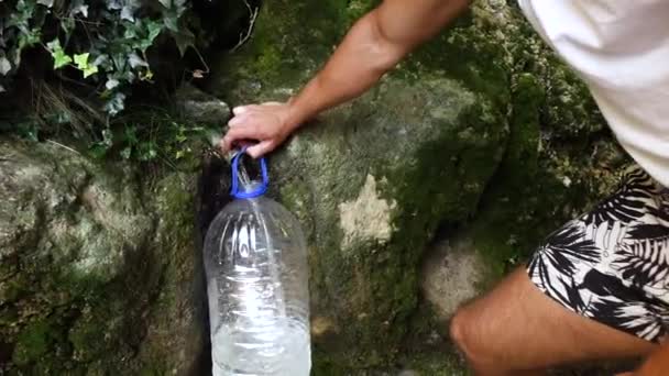 een man verzamelt water in een fles uit een bron - Video