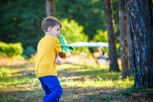 Glückliches Kind, das mit einem Spielzeugflugzeug vor blauem Sommerhimmel spielt. Junge werfen Schaumstoffflugzeug in den Wald oder Park. Bestes Kindheitskonzept. - Foto, Bild
