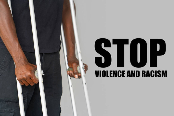 Afrikanischer Mann auf Krücken vor grauem Hintergrund. Das Konzept von Gewalt und Rassismus in den USA und der Welt - Foto, Bild