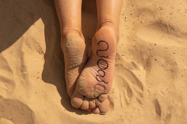 2020 written in marker on a woman's foot against a background of sand - Valokuva, kuva