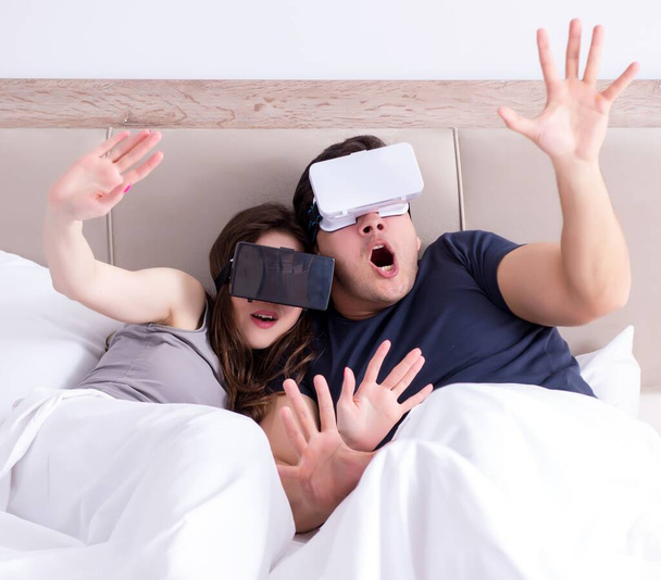 The wife and husband with virtual reality goggles in the bed - Photo, Image