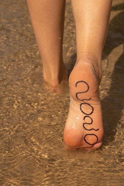 2020 γραμμένο με μαρκαδόρο σε θηλυκό πόδι σε θαλασσινό νερό το καλοκαίρι - Φωτογραφία, εικόνα