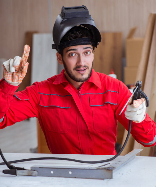 Молодой ремонтник со сварочным электродом и шлемовым сварщиком - Фото, изображение