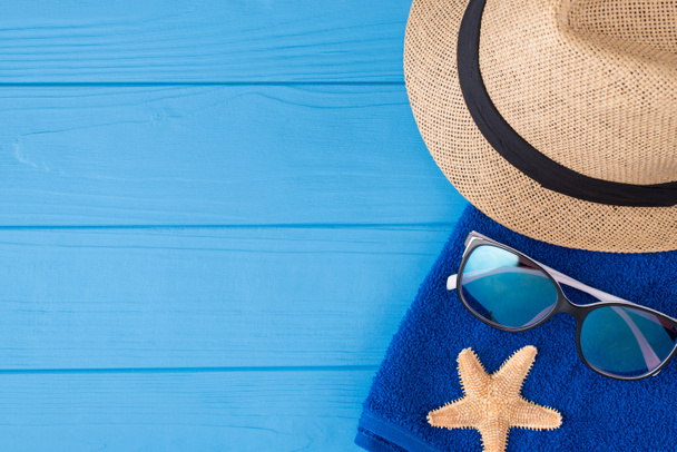 Urlaub am Meer Konzept. Oben über Overhead-Ansicht Nahaufnahme Foto eines Handtuchs Sonnenbrille Seestern und einem Sonnenhut isoliert auf blauem Holzhintergrund mit Kopierraum - Foto, Bild