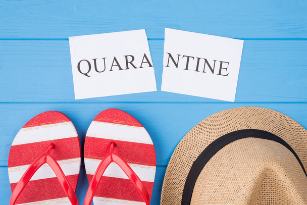 End quarantine concept. Top above overhead view photo of torn word quarantine flipflops and hat isolated on blue wooden background - Photo, Image