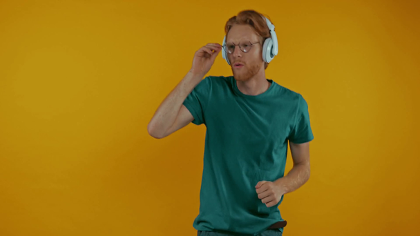 gelukkige roodharige man met koptelefoon loopt geïsoleerd op geel - Video