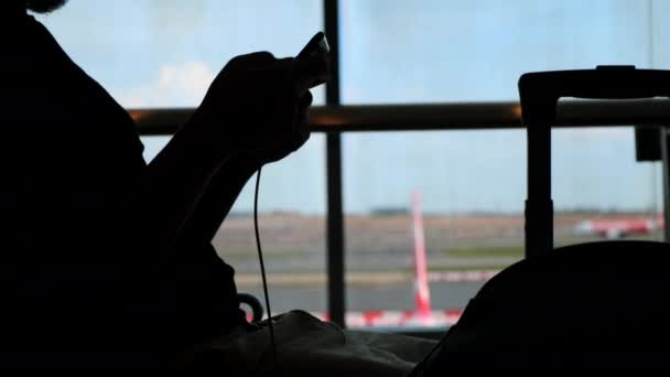 Er langweilt sich beim Warten auf den Flug, Handy hilft, die Zeit abzuwürgen - Filmmaterial, Video