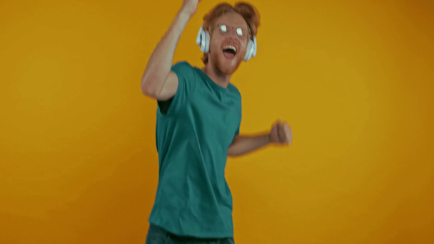 szczęśliwy ruda człowiek w słuchawki taniec odizolowany na żółty - Materiał filmowy, wideo