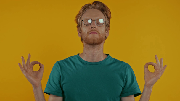 ruhiger Rotschopf mit Brille meditiert isoliert auf gelb - Filmmaterial, Video