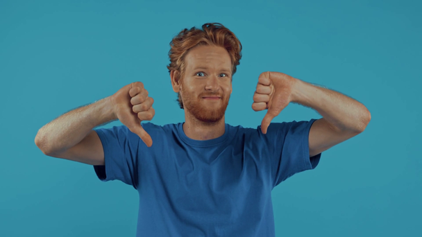 rossa uomo puntando con il dito e mostrando i pollici verso il basso isolato su blu - Filmati, video