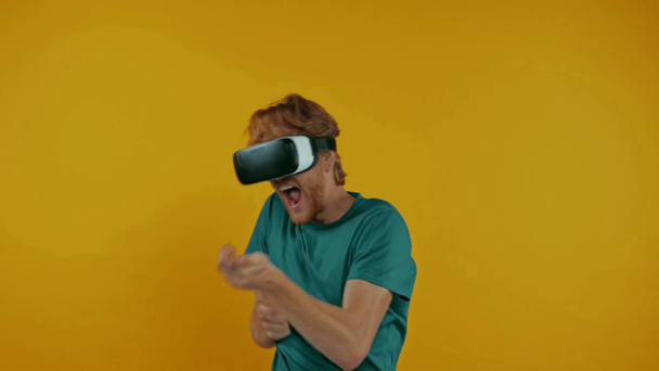 redhead man in vr headset playing shooter game isolated on yellow - Záběry, video