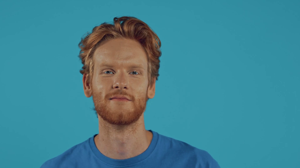 glimlachende roodharige man met baard die rond kijkt geïsoleerd op blauw - Video