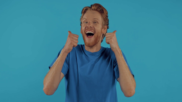 mężczyzna wskazuje palcem, pokazuje kciuki do góry i śmieje się odizolowany na niebiesko - Materiał filmowy, wideo