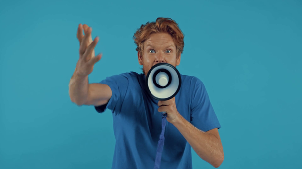 geïrriteerde roodharige met baard schreeuwend in megafoon geïsoleerd op blauw - Video