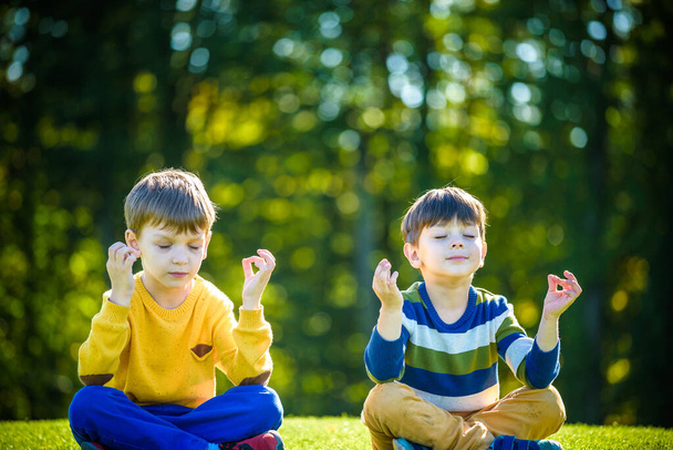 Двоє друзів-кавказьких хлопчиків сидять на свіжому зеленому полі трави і медитують в повсякденному одязі, щасливі діти насолоджуються спокойним літом на вихідних. Спілкування з друзями.. - Фото, зображення