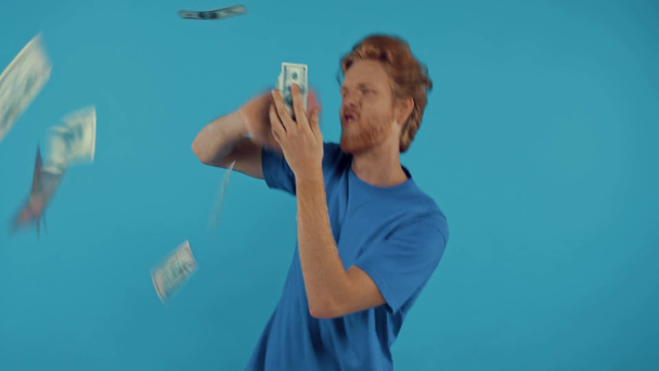 gelukkig rijk roodharige man gooien geld geïsoleerd op blauw - Video
