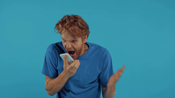 vihainen punapää mies huutaa älypuhelin eristetty sininen - Materiaali, video