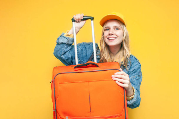 young stylish happy girl tourist with a suitcase smiling on yellow isolated background, travel concept, airplane passenger - Photo, image