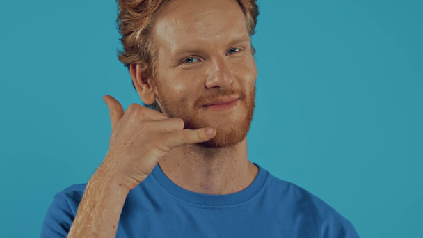 redhead man winking and showing call me gesture isolated on blue - Footage, Video