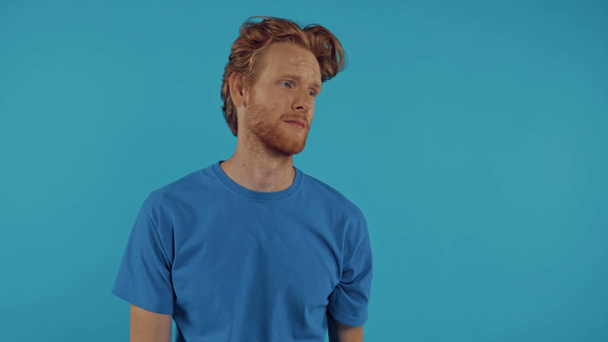 sad redhead man throwing smartphone isolated on blue - Záběry, video