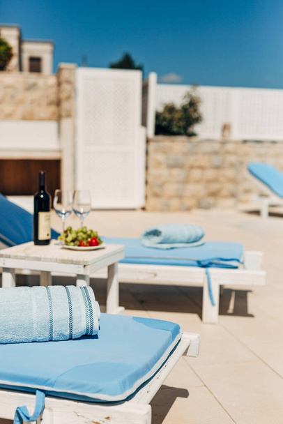 Blaue Handtücher auf Liegestühlen am Strand. Tisch mit Wein, Gläsern und Trauben. - Foto, Bild