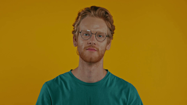 glimlachende roodharige man in bril kijkend naar camera geïsoleerd op geel - Video