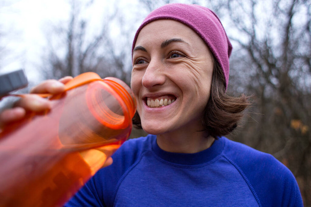 Das Mädchen läuft durch den herbstlichen Wald. Eine Frau trainiert in der Natur. Läufer bereitet sich auf den Marathon vor. Ausdauer. Mädchen trinkt Wasser nach dem Joggen. Sportbekleidung zum Joggen in der kalten Jahreszeit. - Foto, Bild