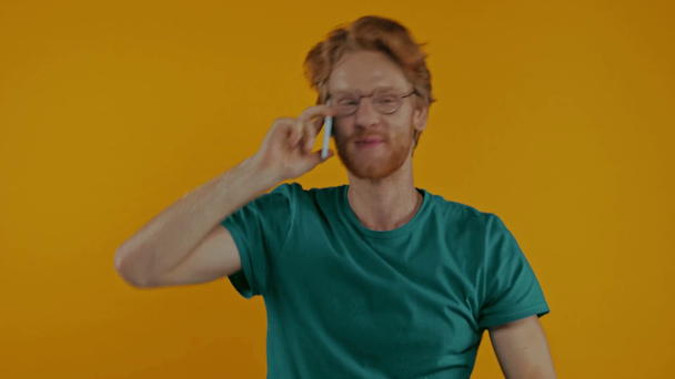 positiivinen punapää mies lasit puhuu älypuhelimella eristetty keltainen - Materiaali, video
