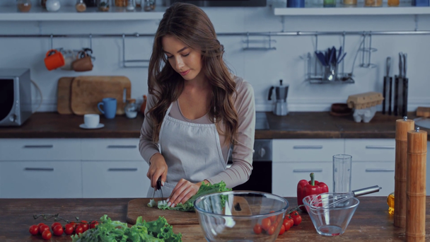 attractive girl in apron cutting lettuce on chopping board  - Filmati, video