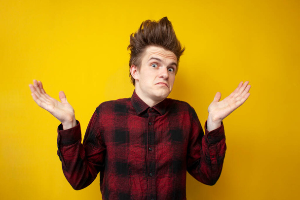 young guy shrugs on yellow isolated background, hipster with funny hairstyle at a loss - Photo, Image