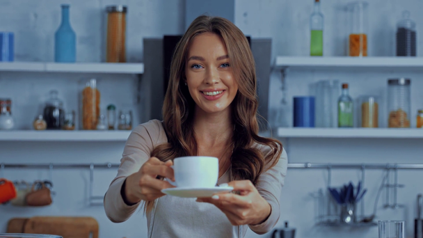 コーヒーとソーサーでカップを持っているエプロンの陽気な女性  - 映像、動画