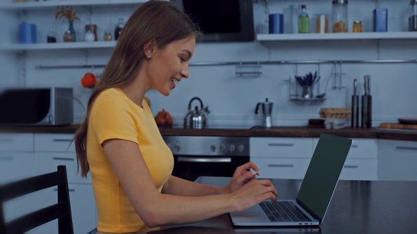 боковой вид привлекательной девушки, улыбающейся во время игры на ноутбуке  - Кадры, видео