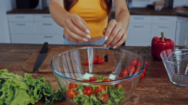 przycięty widok kobiety wprowadzenie pomidorów wiśniowych do miski z sałatą - Materiał filmowy, wideo