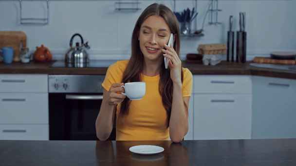 счастливая женщина пьет кофе и разговаривает на смартфоне  - Кадры, видео