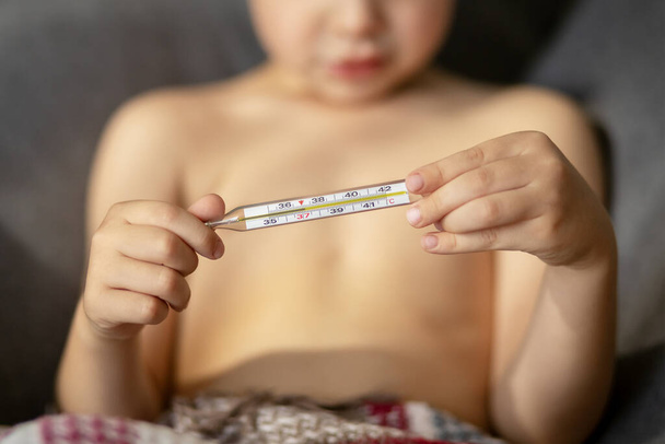 Un termómetro de vidrio cercano muestra una temperatura de treinta y siete grados. Las manos del niño sostienen un termómetro. Medición de temperatura
 - Foto, imagen