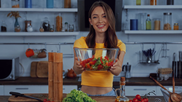 happy woman holding bowl with fresh salad in kitchen - Filmati, video