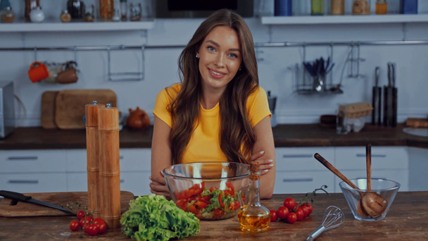 happy woman looking at camera near fresh salad on table - Video