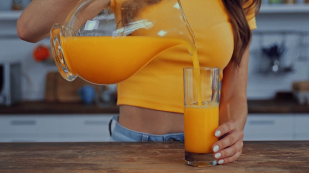 przycięty widok kobiety wylewanie soku pomarańczowego w szkle - Materiał filmowy, wideo